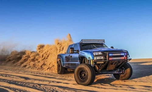 <img src= "chevy_pre_runner.jpg" alt= "a blue chevy pre-runner throws a rooster tail as it speeds around a bend in the course" />